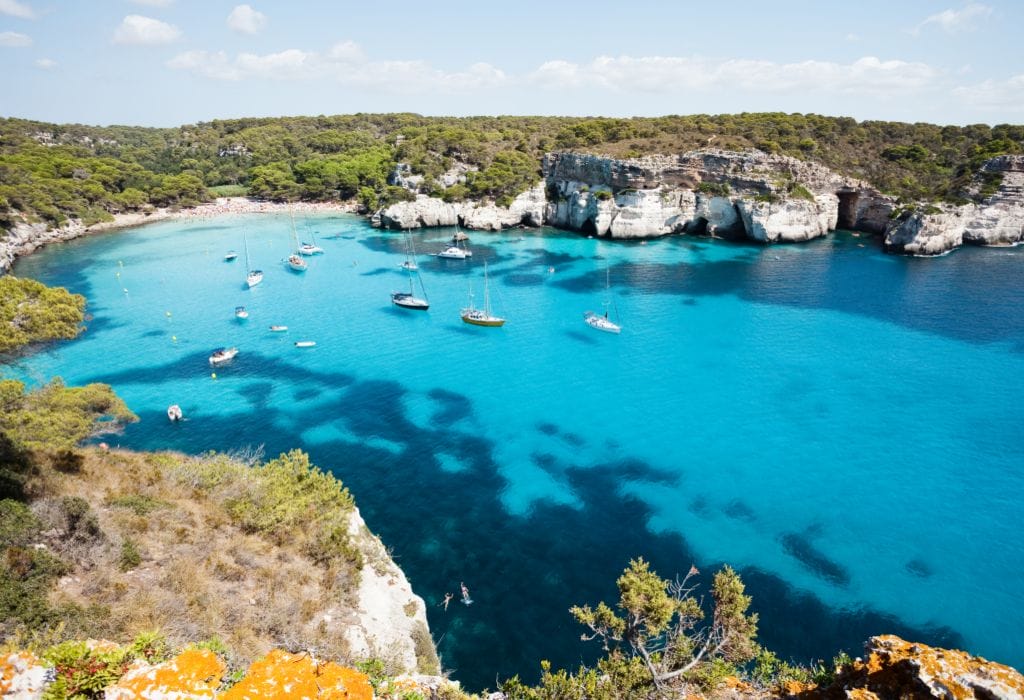 Cala Macarella bay with boats and green-covered cliffs, Menorca, Spain