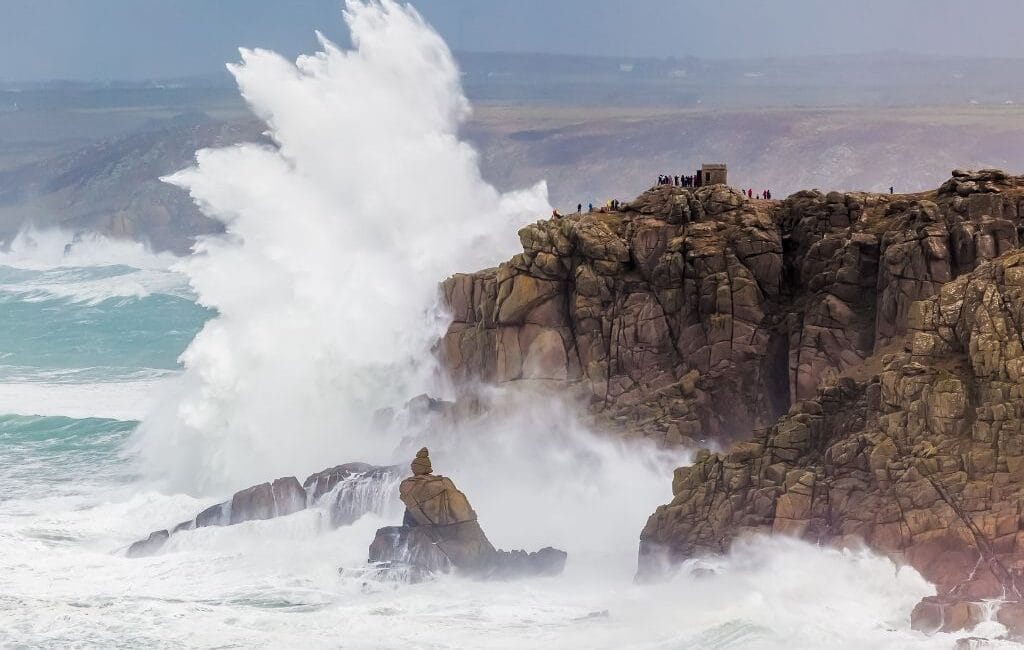 A surfer catching a wave at Sennen Cove with the picturesque Cornwall coastline in the background