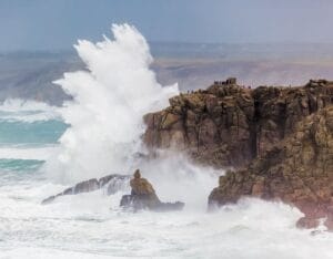 A surfer catching a wave at Sennen Cove with the picturesque Cornwall coastline in the background