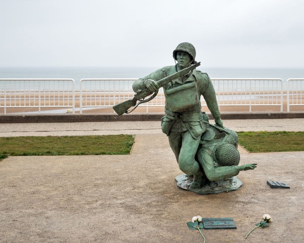 Statue of a soldier rescuing another soldier with the beach and sea in the background in Normandy