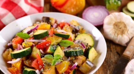 A beautifully arranged plate of traditional Ratatouille with thinly sliced vegetables, including zucchini, eggplant, and bell peppers, baked to perfection with a golden finish.